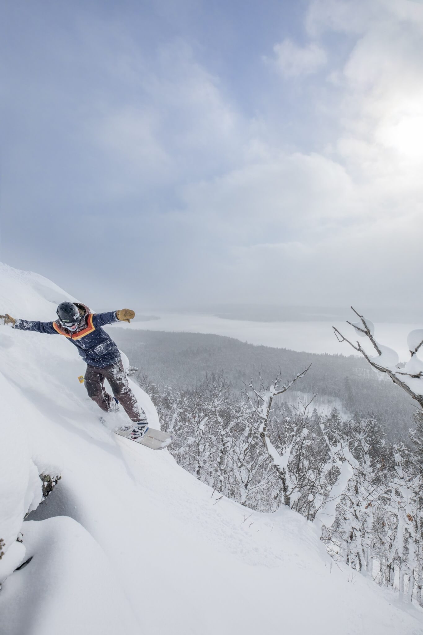 Snowboarder at Mount Bohemia slashing a powder turn with Lake Superior behind them