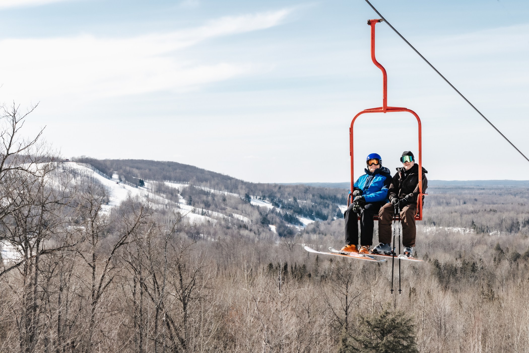 two skiers on chairlift at Jackson Creek Summit with Black River Basin in the distance