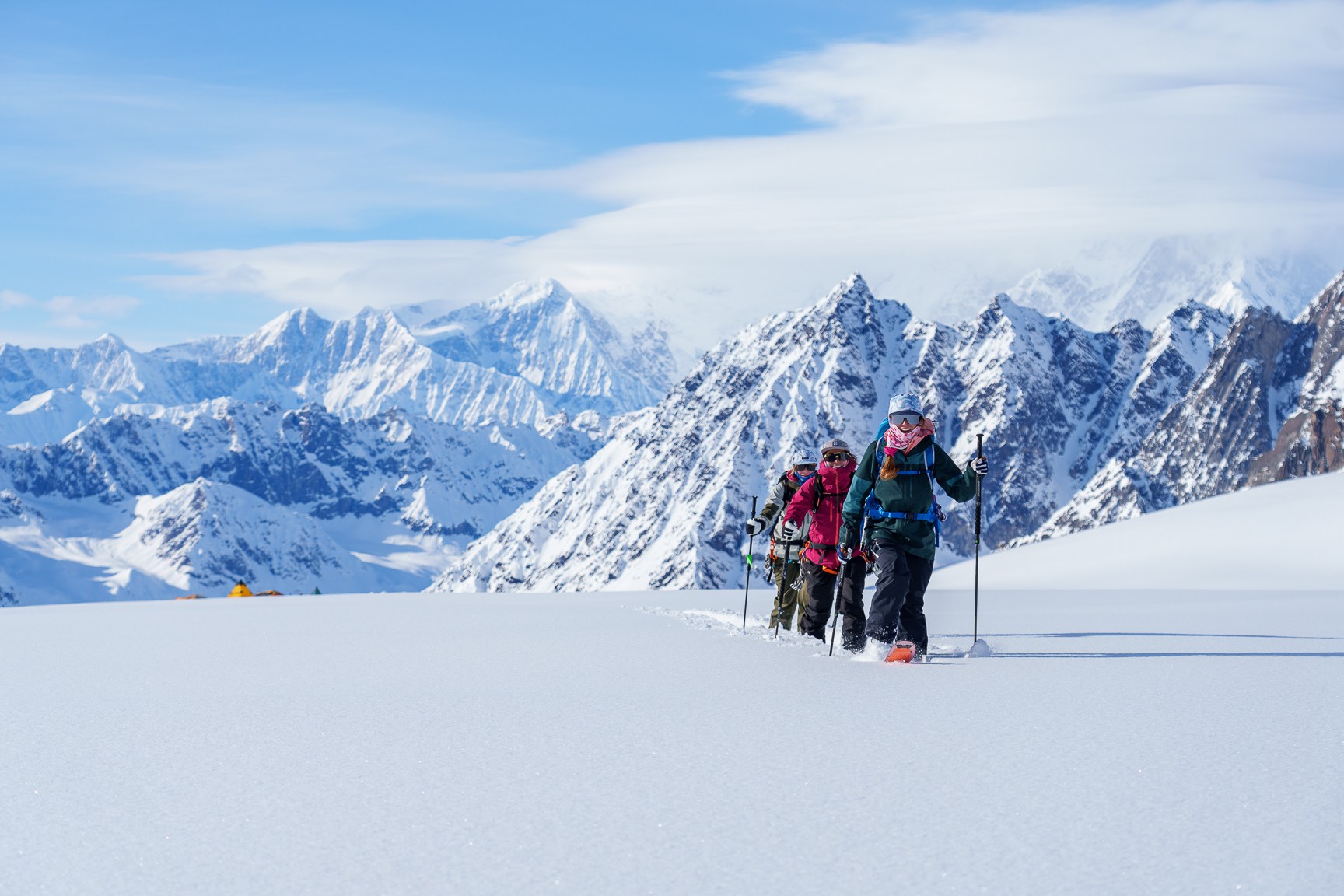 three women backcountry skiing in Alaska with huge mountains behind them