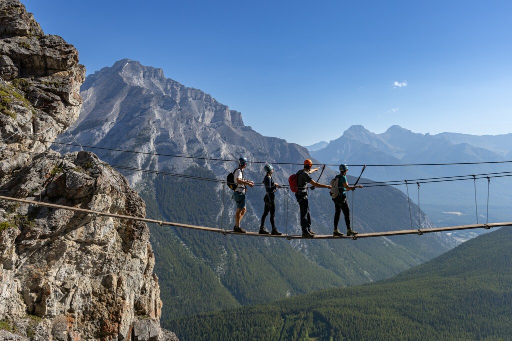 four adventurous souls going over a dangling line at Banff Via Ferrata at Mt Norquay ski resort in Alberta Canada
