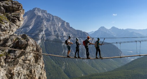 four adventurous souls going over a dangling line at Banff Via Ferrata at Mt Norquay ski resort in Alberta Canada