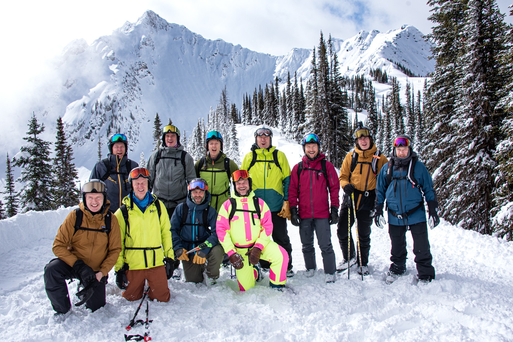 Group of skiers and snowboarders with Goat Range in the Selkirk Mountains behind them