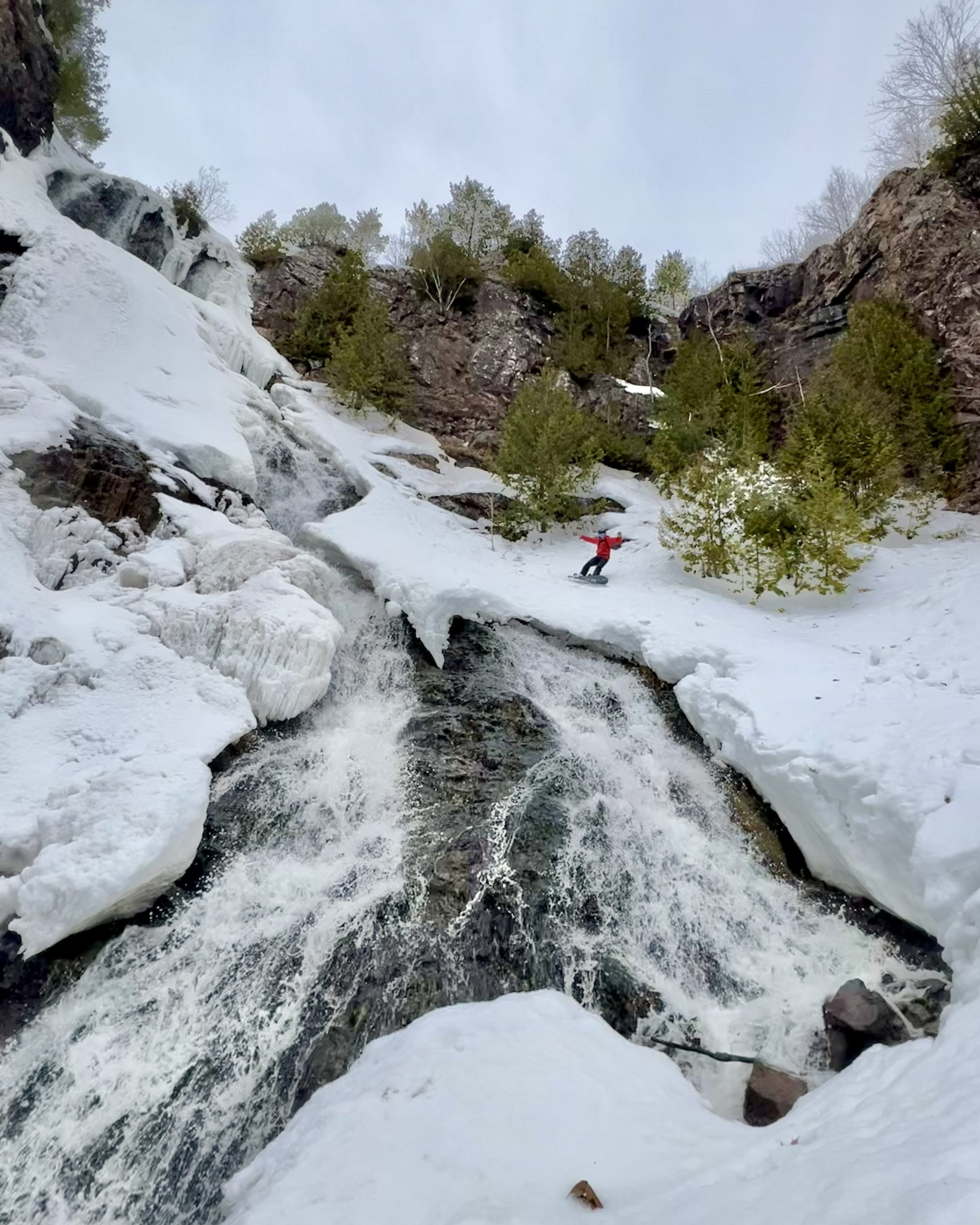 Snowboarder riding next to Houghton-Douglass Falls in Michigan